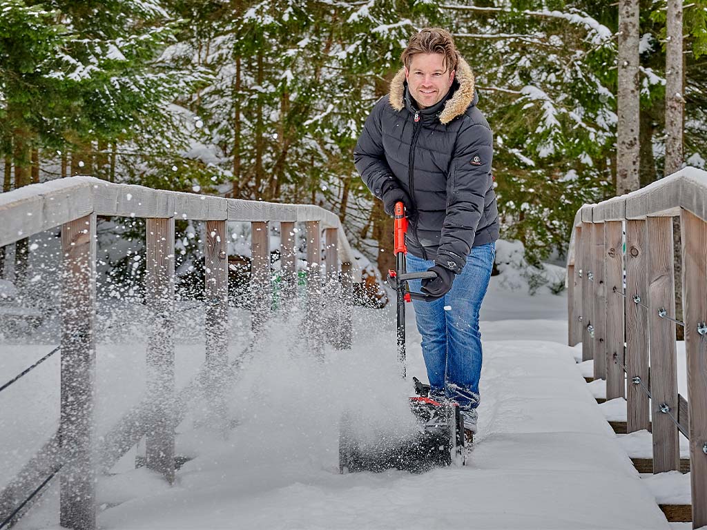 Man clearing snow with a red snow blower in front of a yellow house