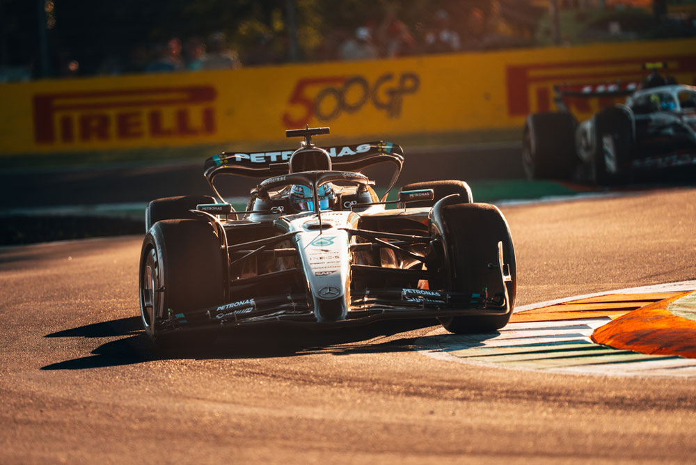 Automobil Mercedes-AMG PETRONAS Formula One tima vozi po sunčanoj stazi tijekom Velike nagrade. Automobil ulazi u zavoj velikom brzinom, dok se u pozadini vidi drugo vozilo.