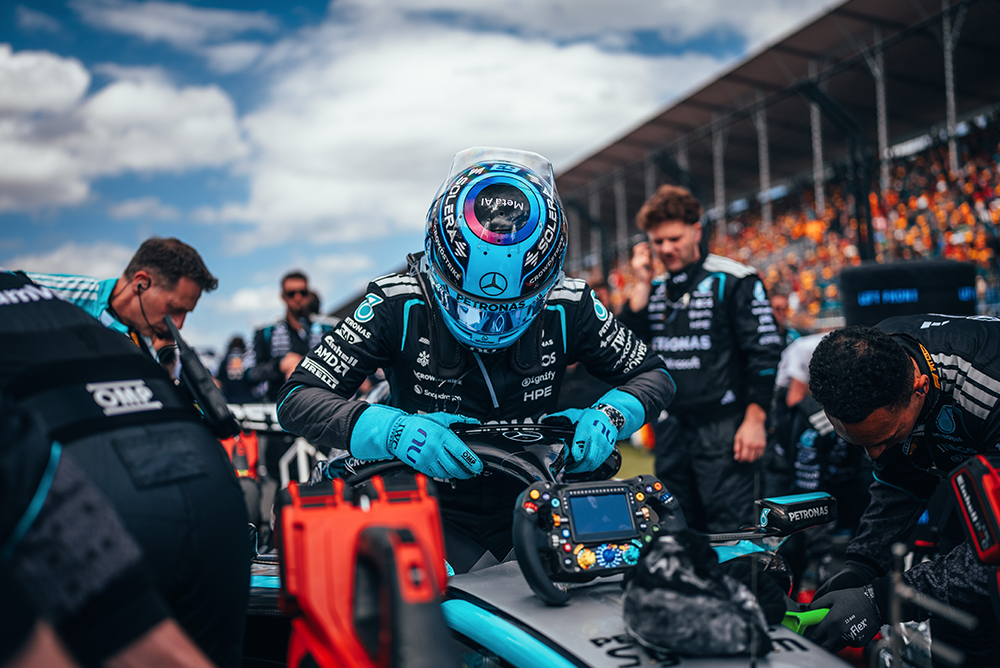 Vozač Formule 1 sjedi u bolidu okružen timom na стартној решетки.