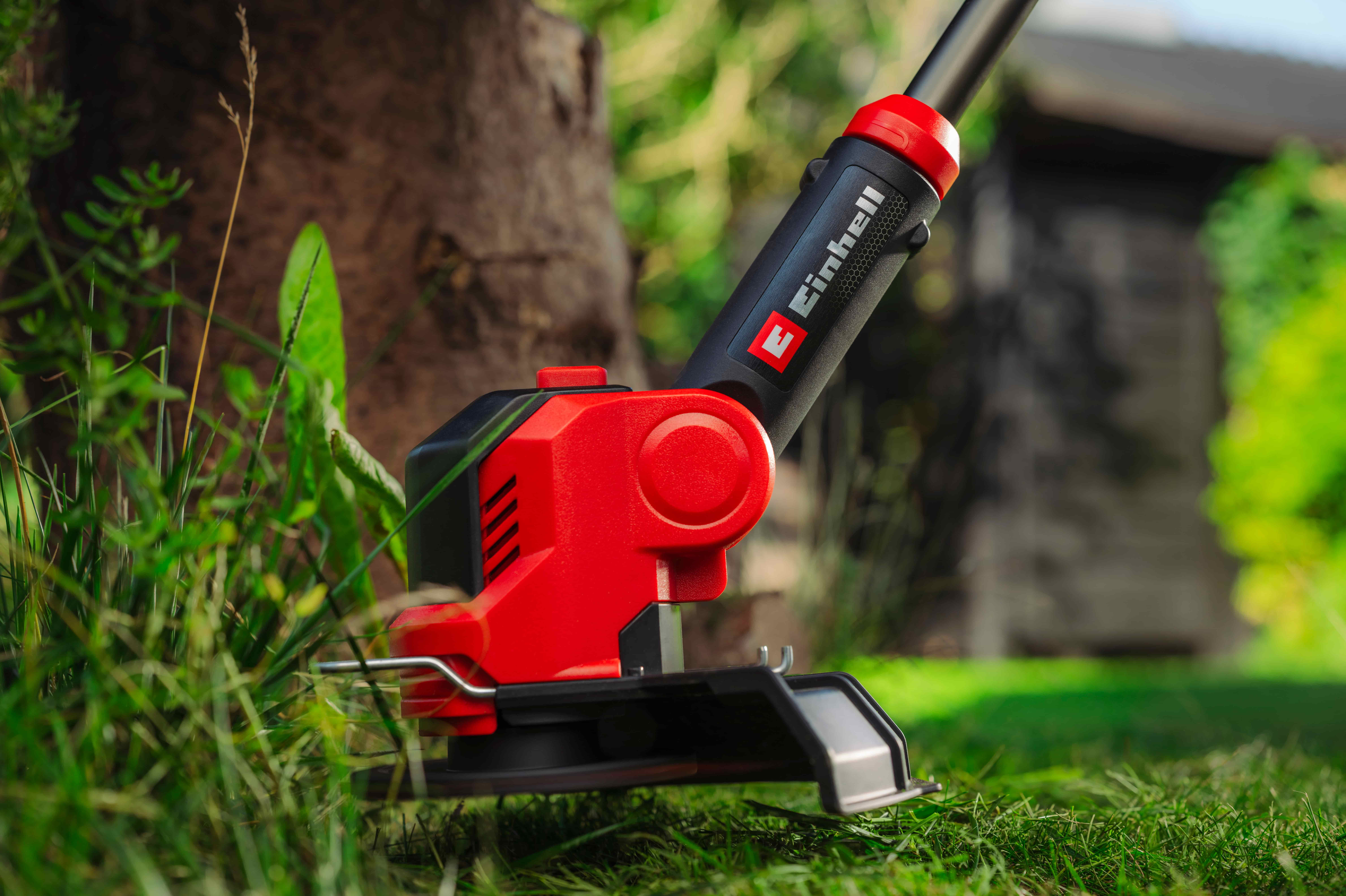 Einhell trimer podrezuje travu oko stabla u vrtu.