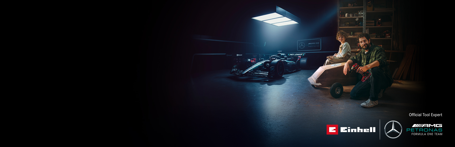 Otac i dijete u radionici s domaćim soapbox automobilom. U pozadini se nalazi Mercedes-AMG PETRONAS Formula 1 bolid i Einhell alati.