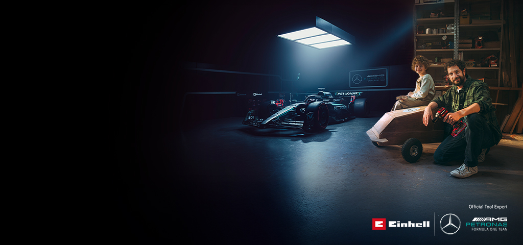 Otac i dijete u radionici s domaćim soapbox automobilom. U pozadini se nalazi Mercedes-AMG PETRONAS Formula 1 bolid i Einhell alati.
