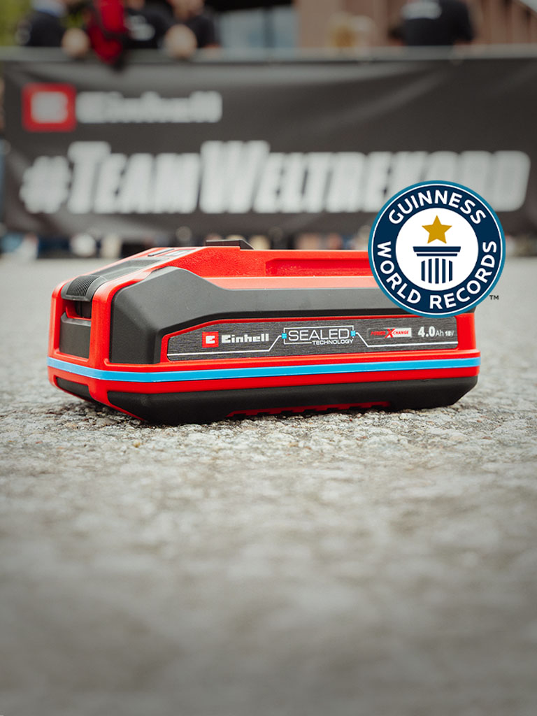 Einhell SEALED battery Power X-Change 4.0 Ah lies on asphalt, with the Guinness World Records "Record Holder" logo on the right.