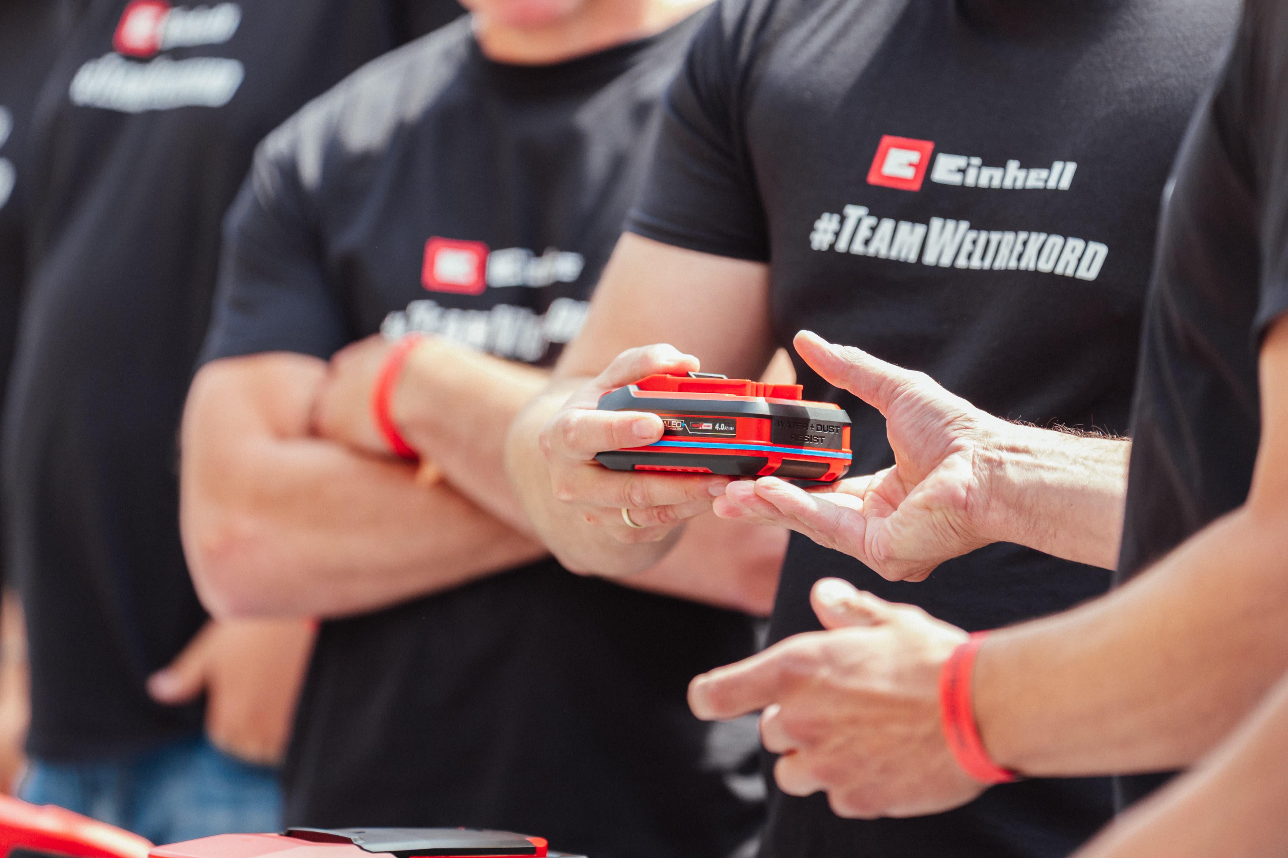 Close-up of the handover of an Einhell SEALED battery Power X-Change 4.0 Ah between two people.