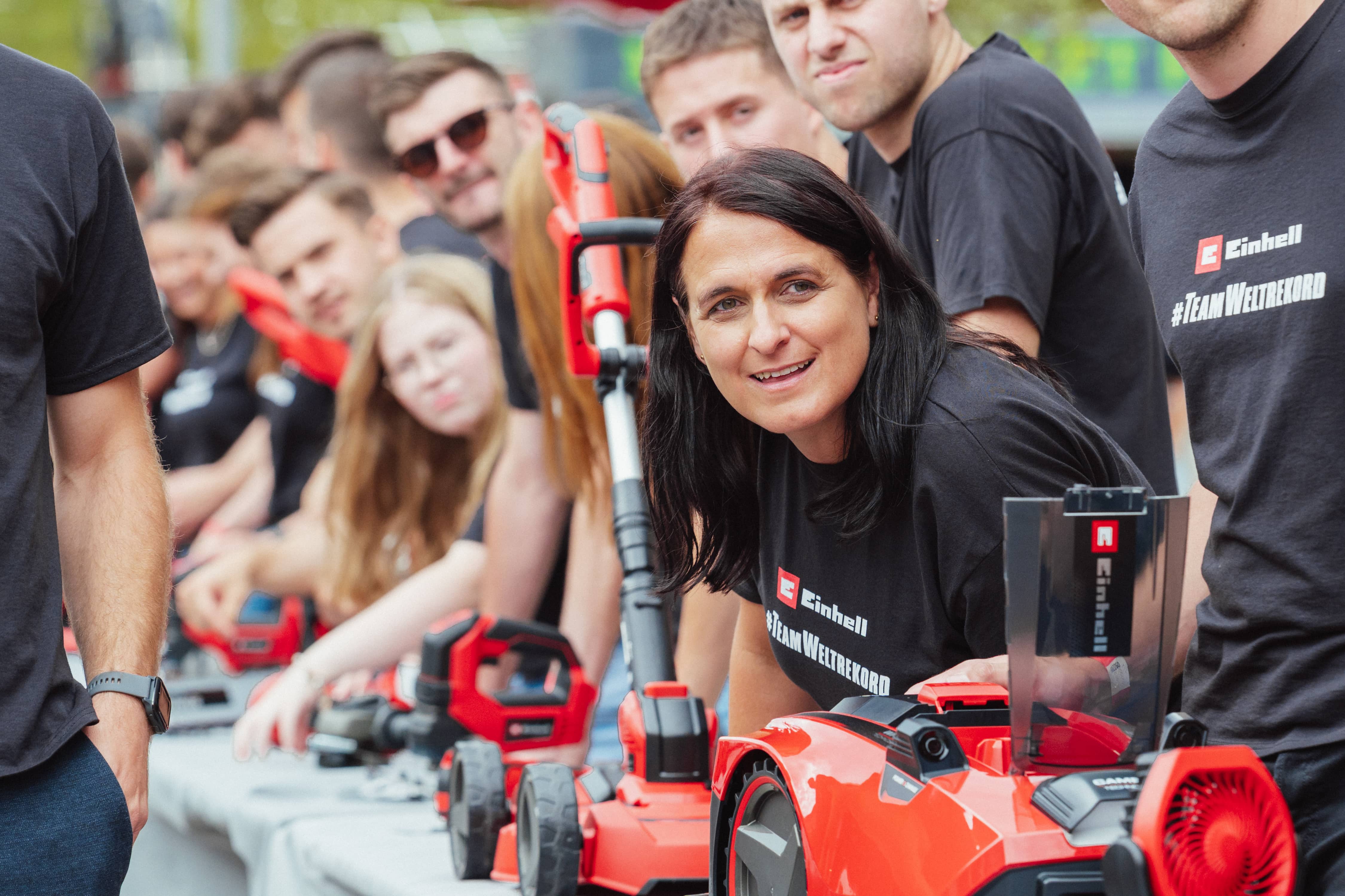 A woman leans forward smiling at the camera, surrounded by other Einhell employees and tools.