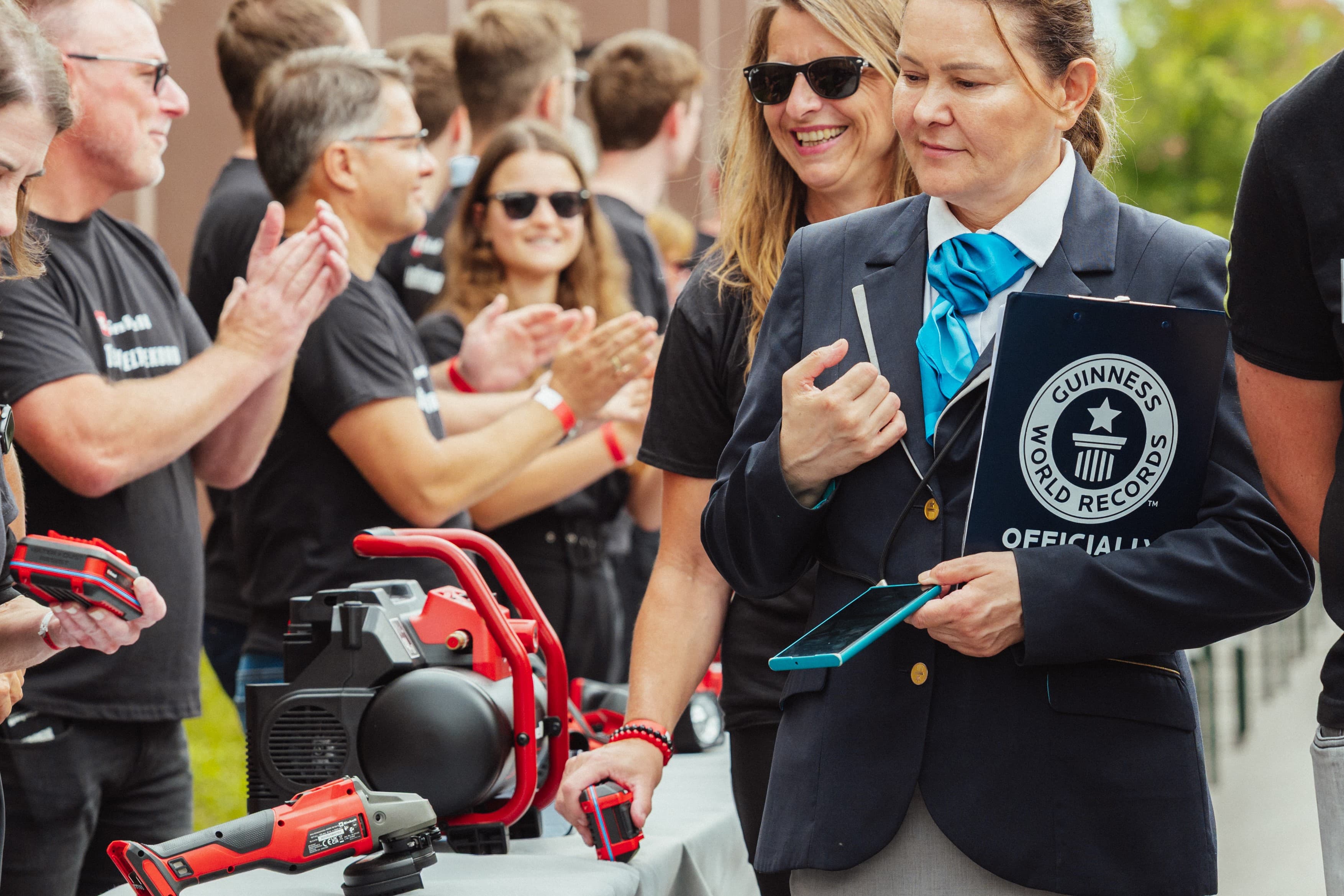 A Guinness representative with clipboard stands next to applauding people at a table with Einhell tools.