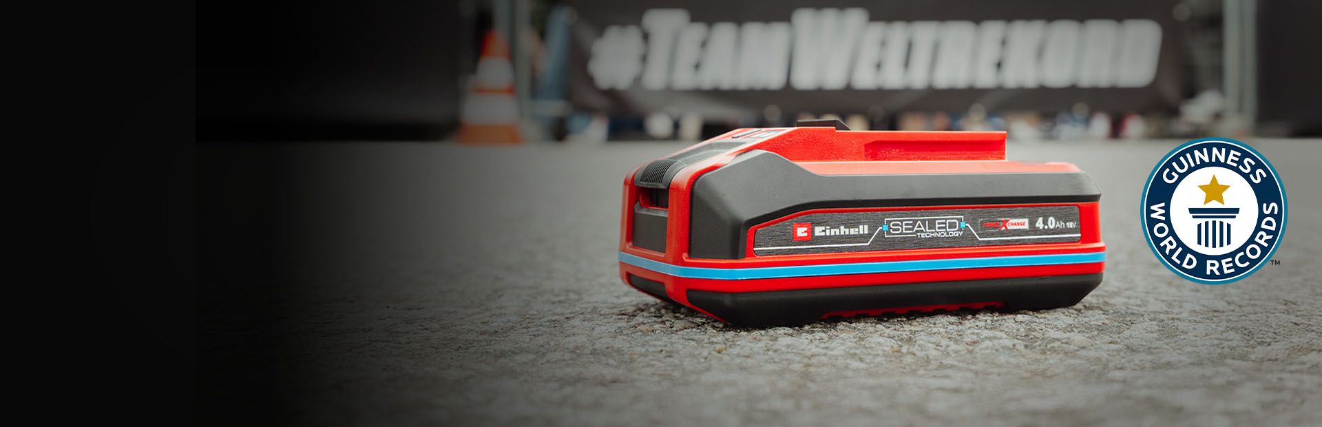 Einhell SEALED baterija Power X-Change 4.0 Ah leži na asfaltu, s Guinness World Records logotipom "Record Holder" s desne strane.