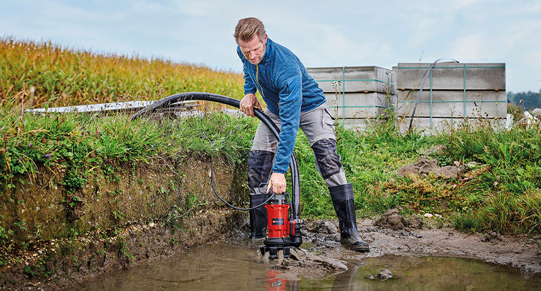 A man pumping out a large, dirty puddle of water with the help of a dirty water pump.