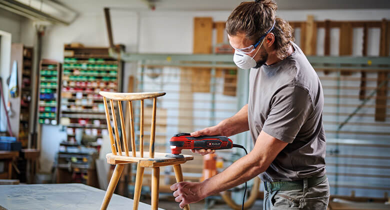 A man grinds the seat of a chair with a corded multifunction device from Einhell.