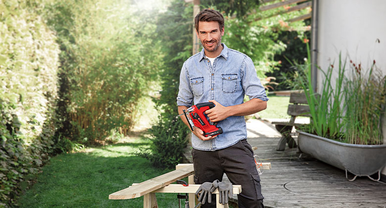 A man standing in the garden with a cordless jigsaw in his hands